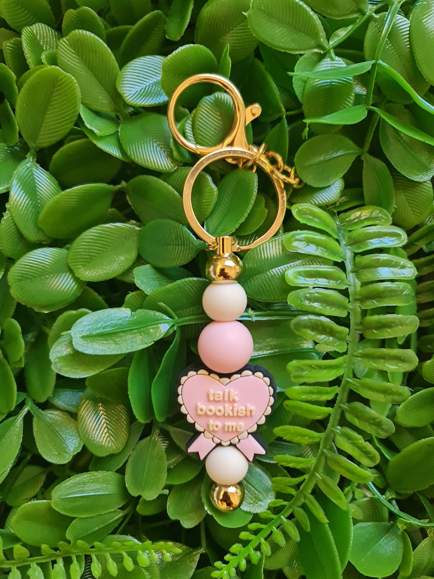 Decorative keychain with pink and gold elements on a green leaf background