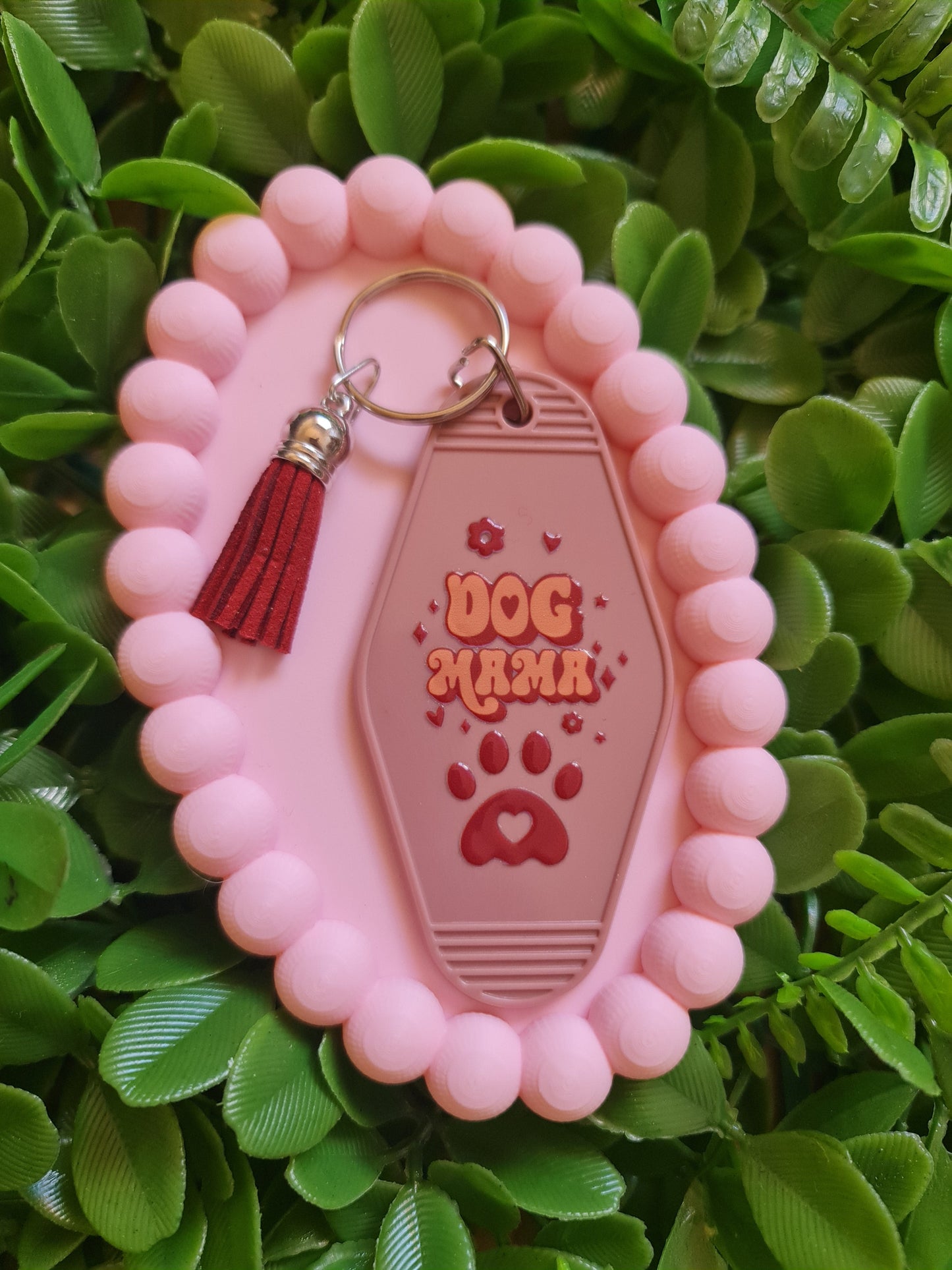 Pink dog tag holder with a red tassel on a green leafy background