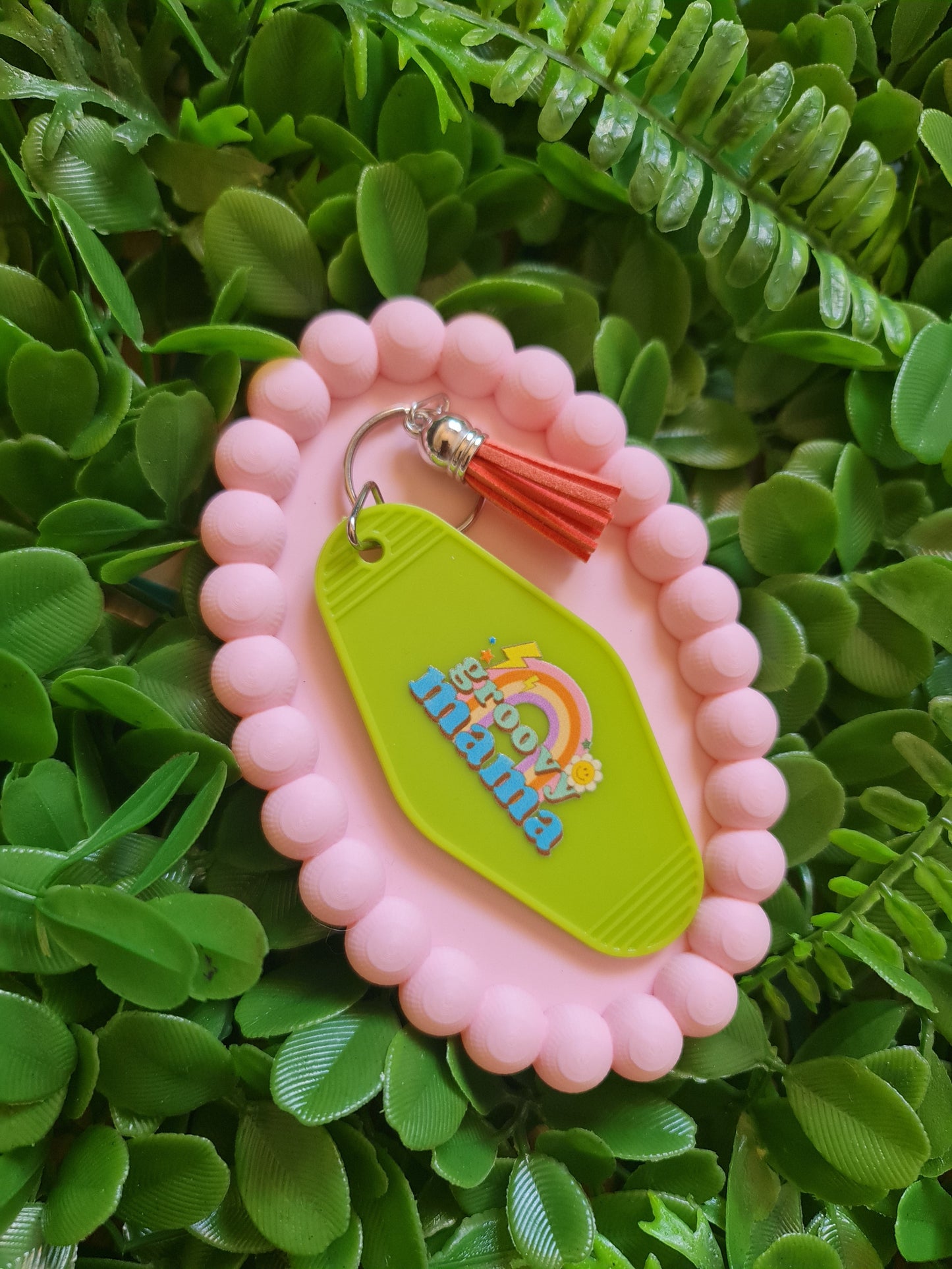 Pink case with a green tag featuring 'mama' and a rainbow design, on a green leafy background.