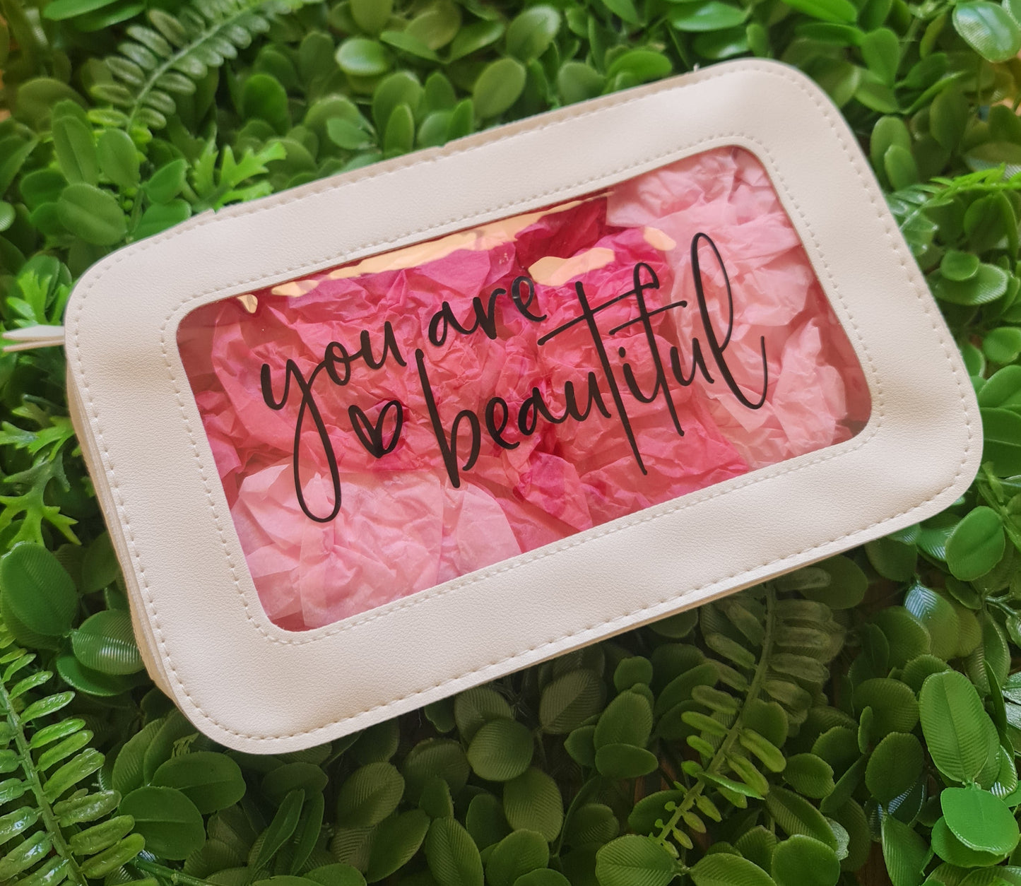 Pink makeup palette with 'you are beautiful' text on a green leafy background