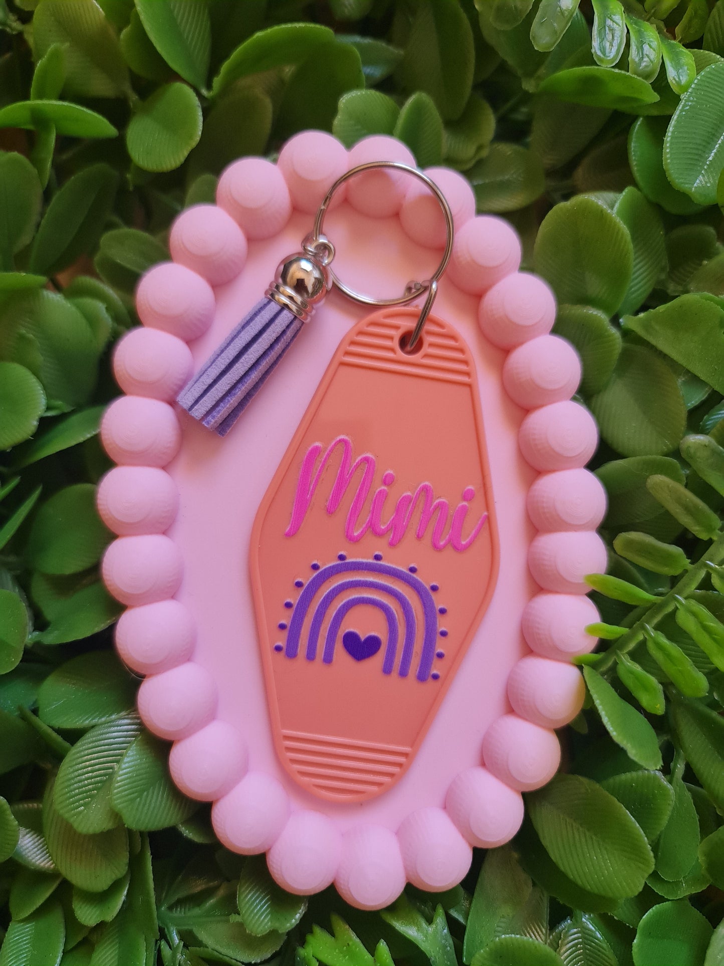 Pink and orange keychain with 'Mimi' branding on a green leafy background