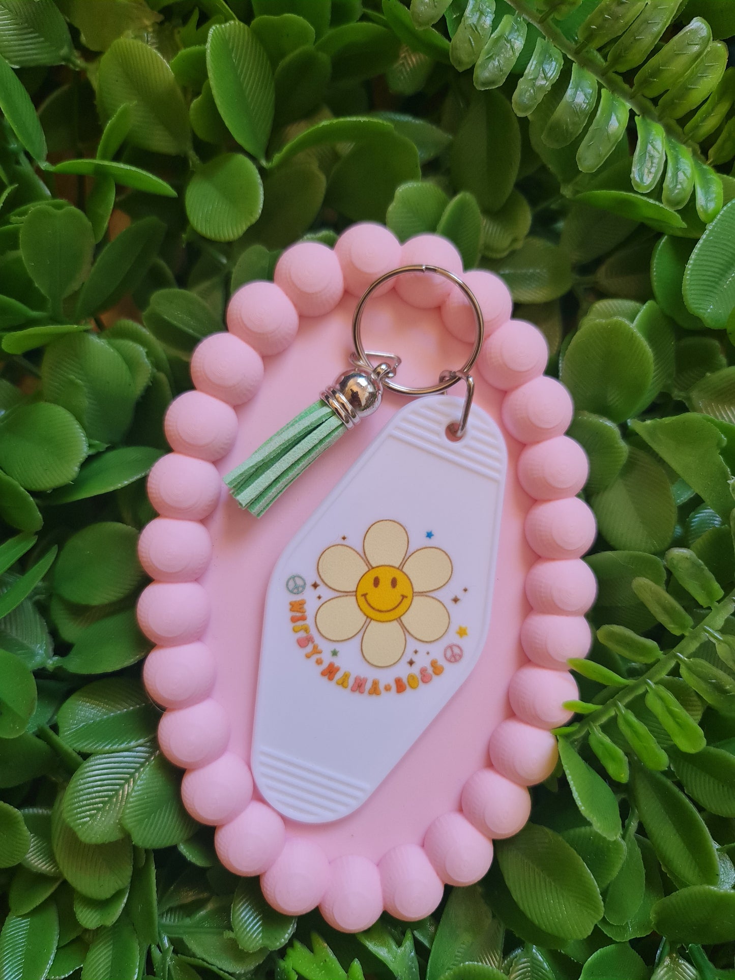 Pink keychain holder with a keychain featuring a flower design on a green leafy background