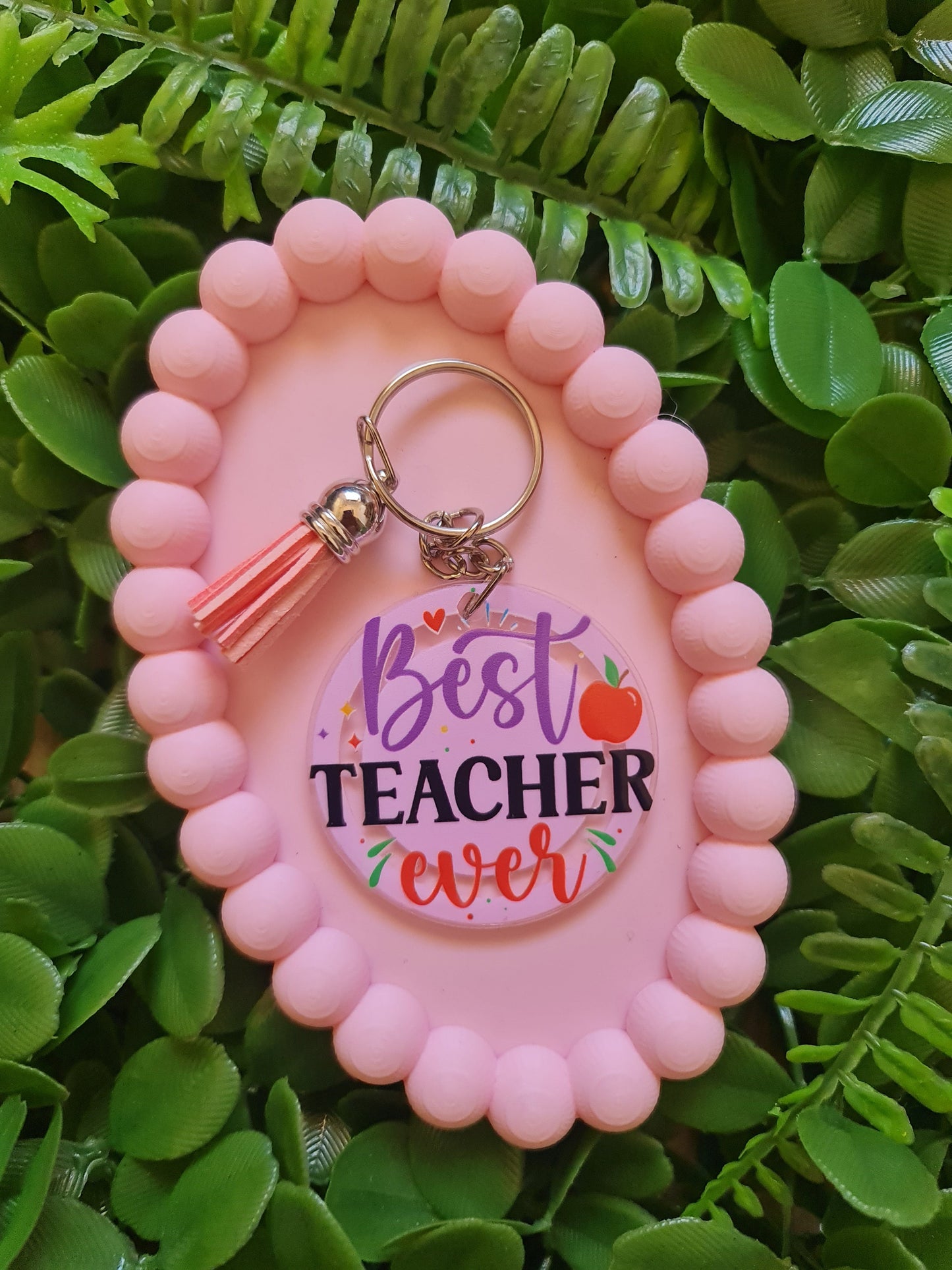 Pink keychain holder with 'Best Teacher Ever' keychain on green leaves