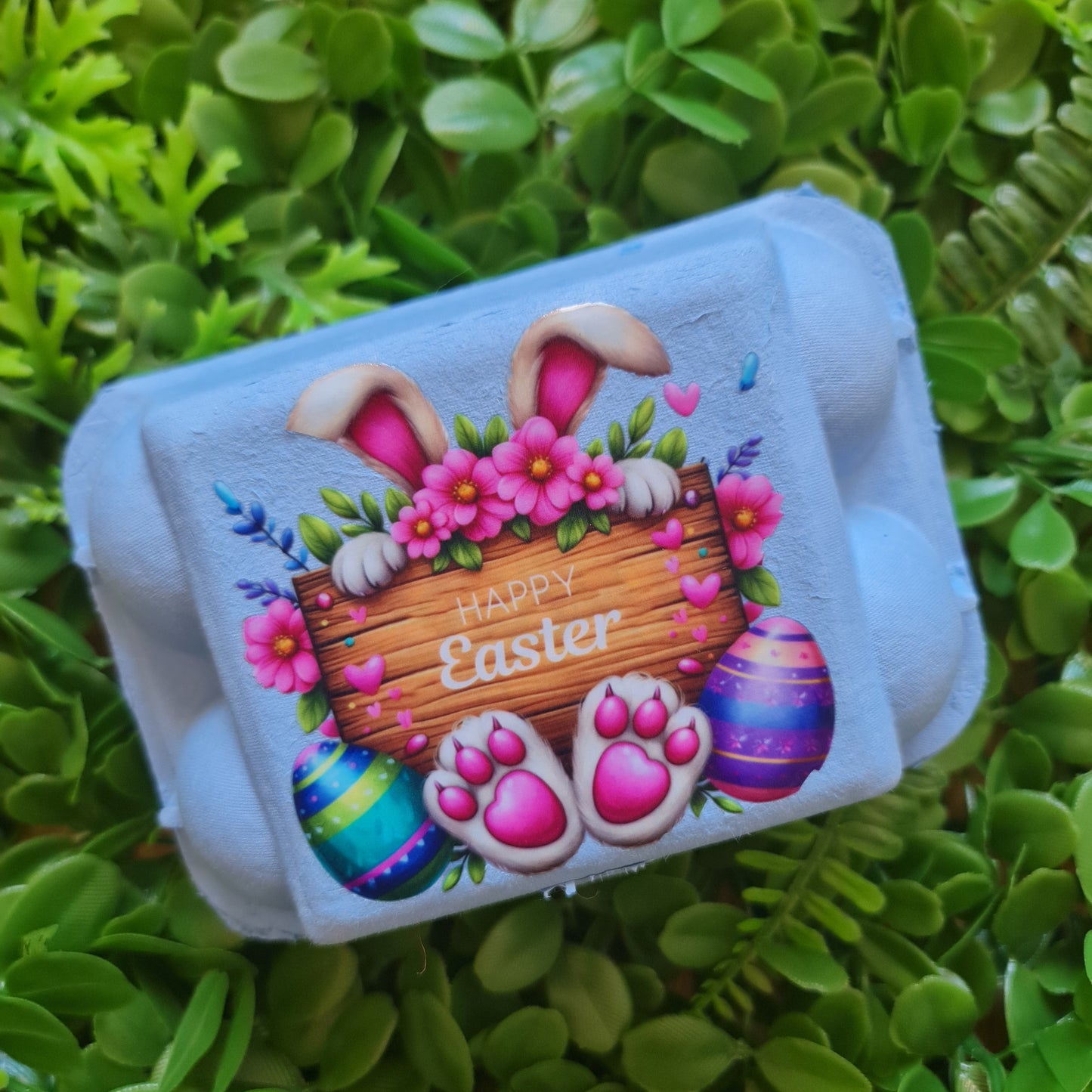 Carton of Easter-themed eggs with a bunny and eggs design on green grass.