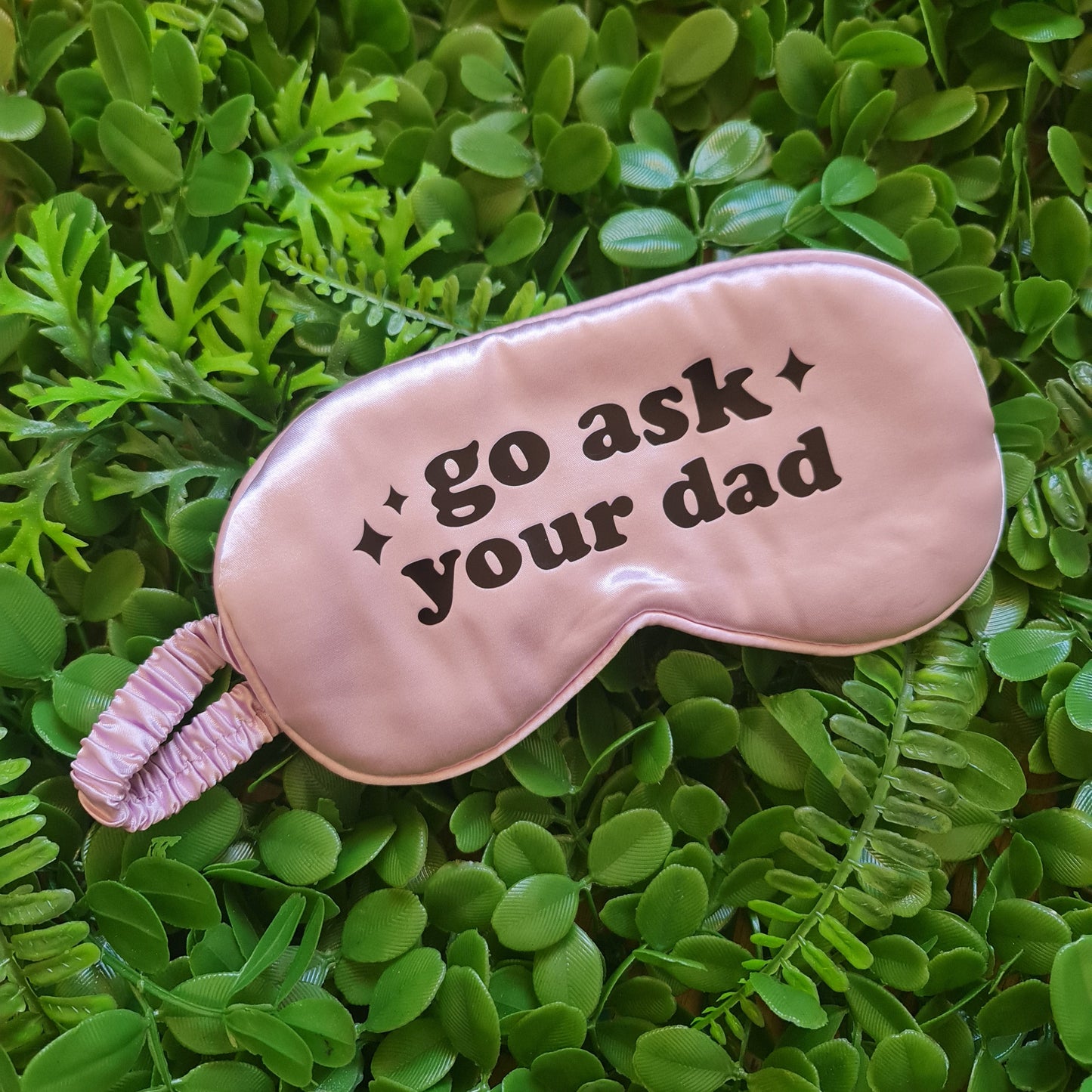Pink sleep mask with text on a green leafy background