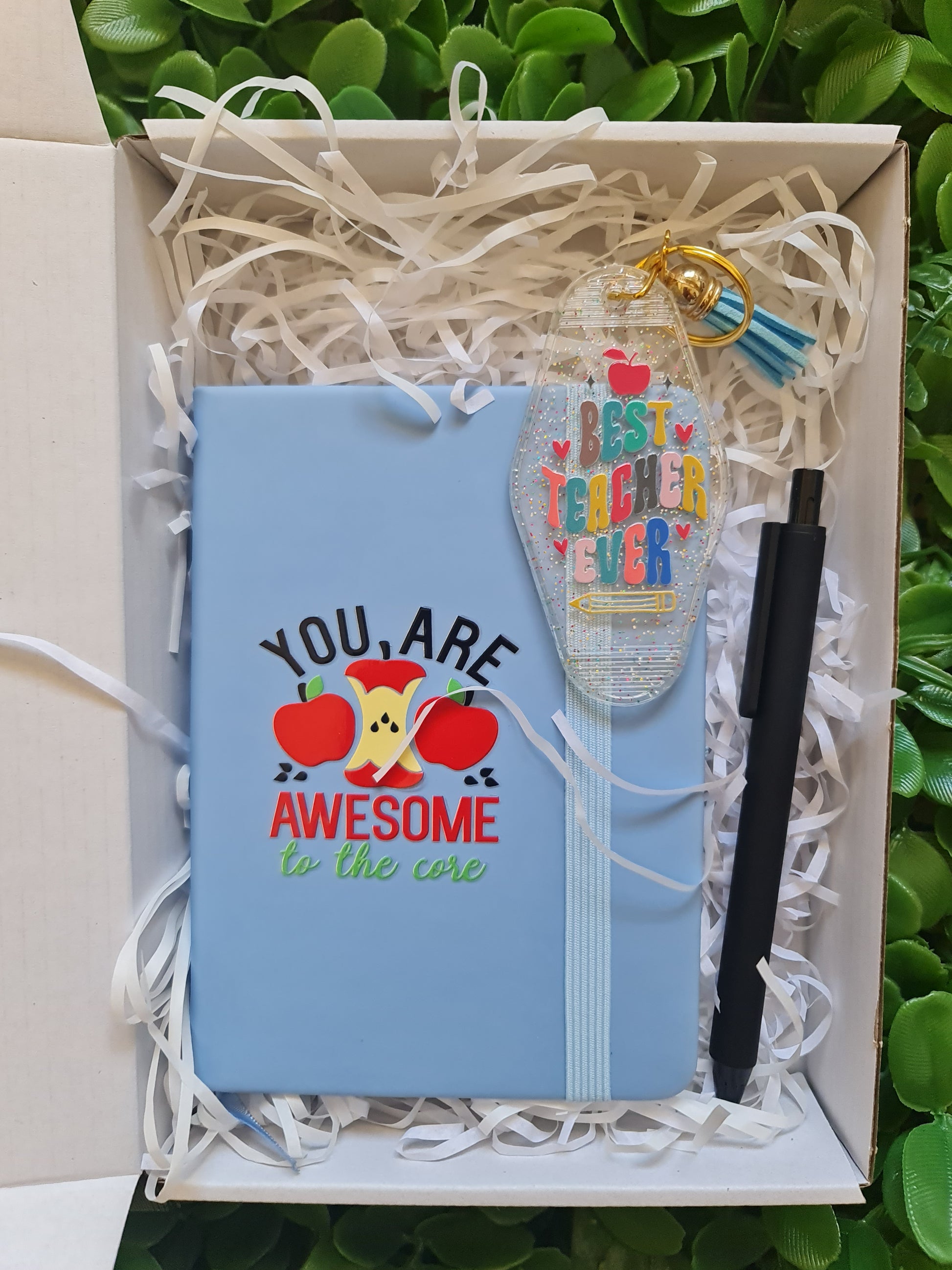 Gift set with a notebook, pen, and keychain in a box with greenery in the background