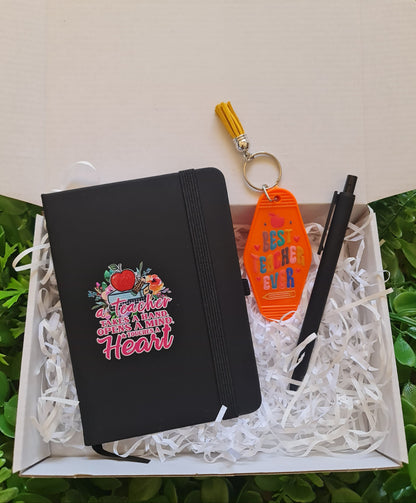Black pouch with colorful text and graphics, orange keychain with colorful design, and black pen in a white box on grass.