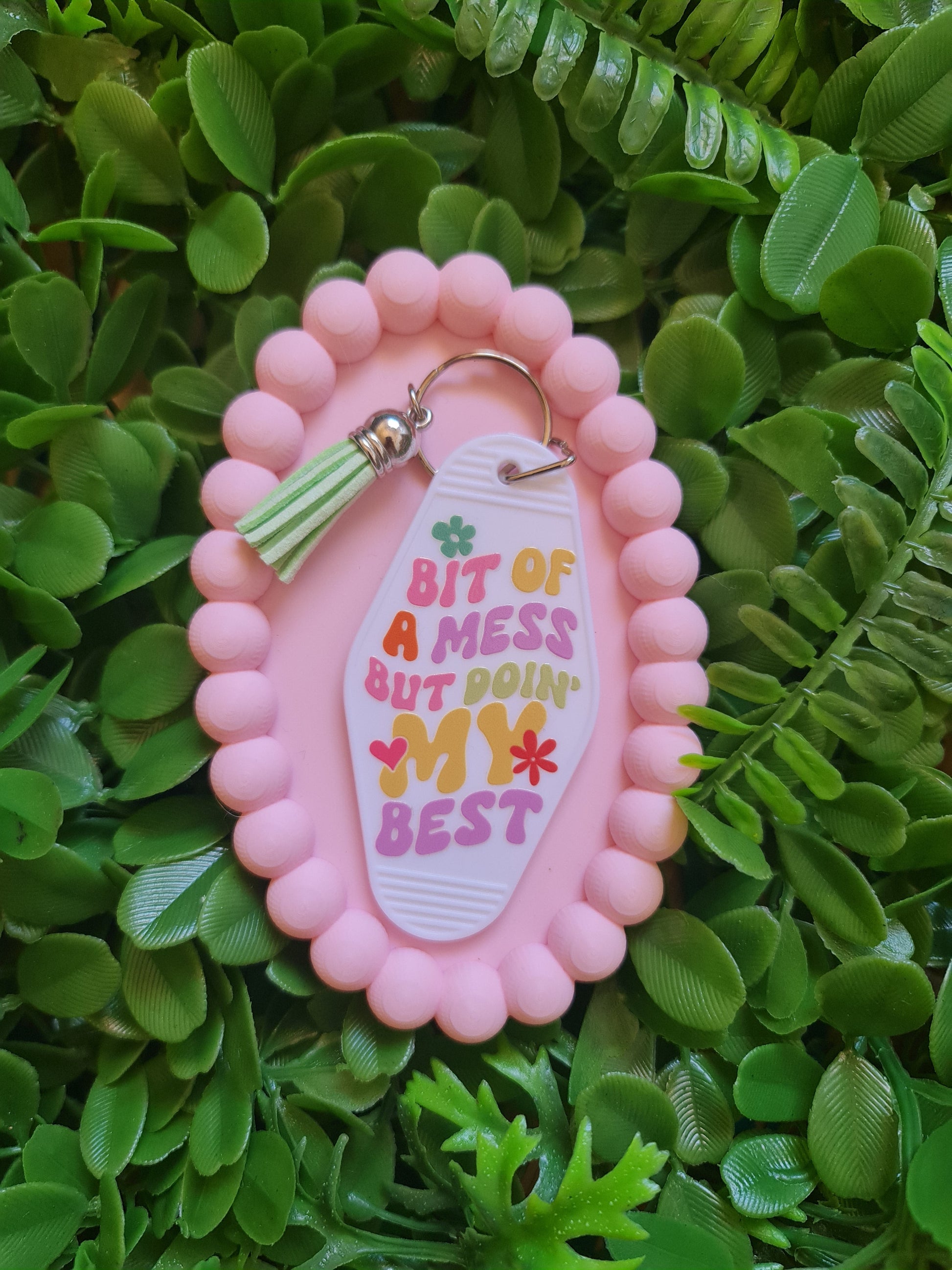 Pink keychain with a colorful tag on a green leafy background