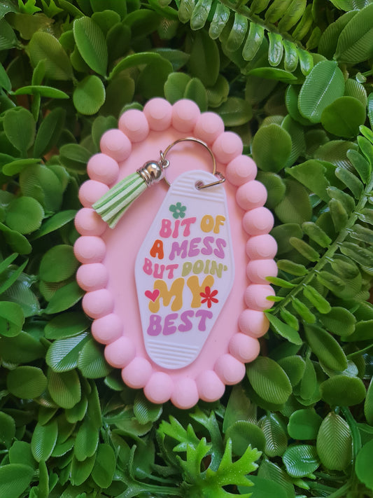 Pink keychain with a colorful tag on a green leafy background