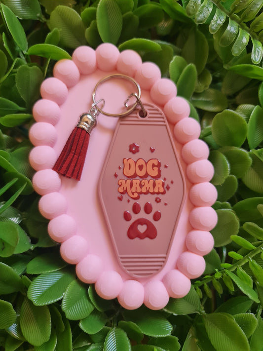 Pink dog tag holder with a red tassel on a green leafy background