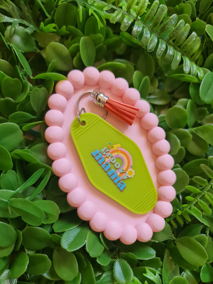 Pink case with a green tag featuring 'mama' and a rainbow design, on a green leafy background.