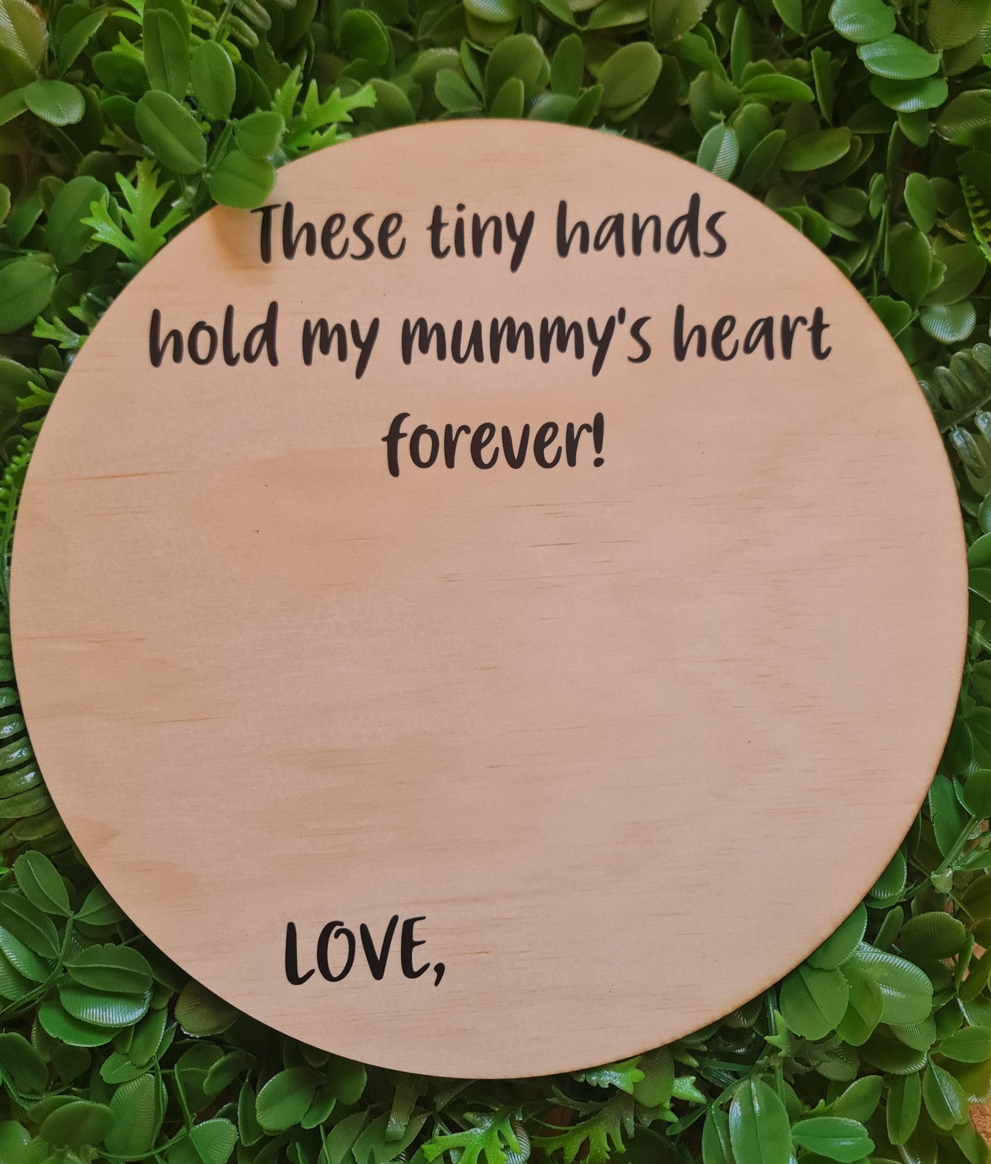 Round wooden plaque with engraved text on a green leafy background
