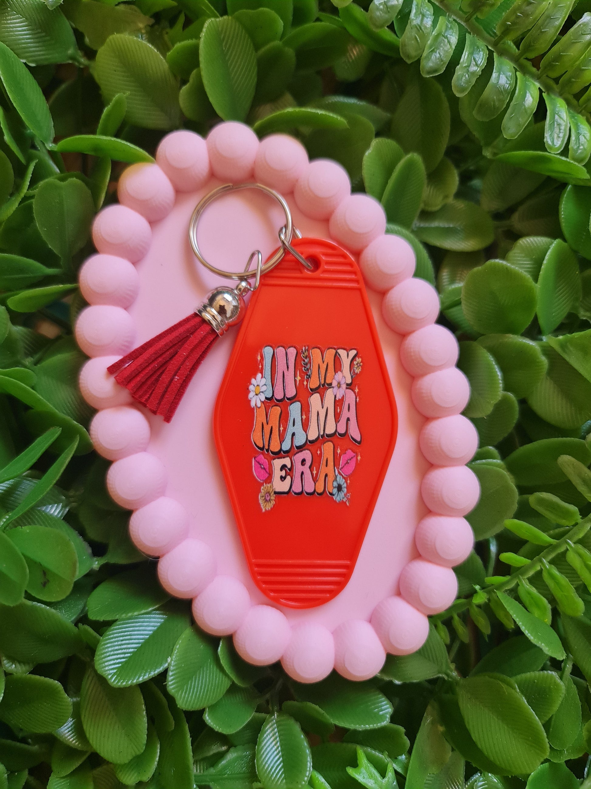 Pink keychain with red tag and tassel on green leaves