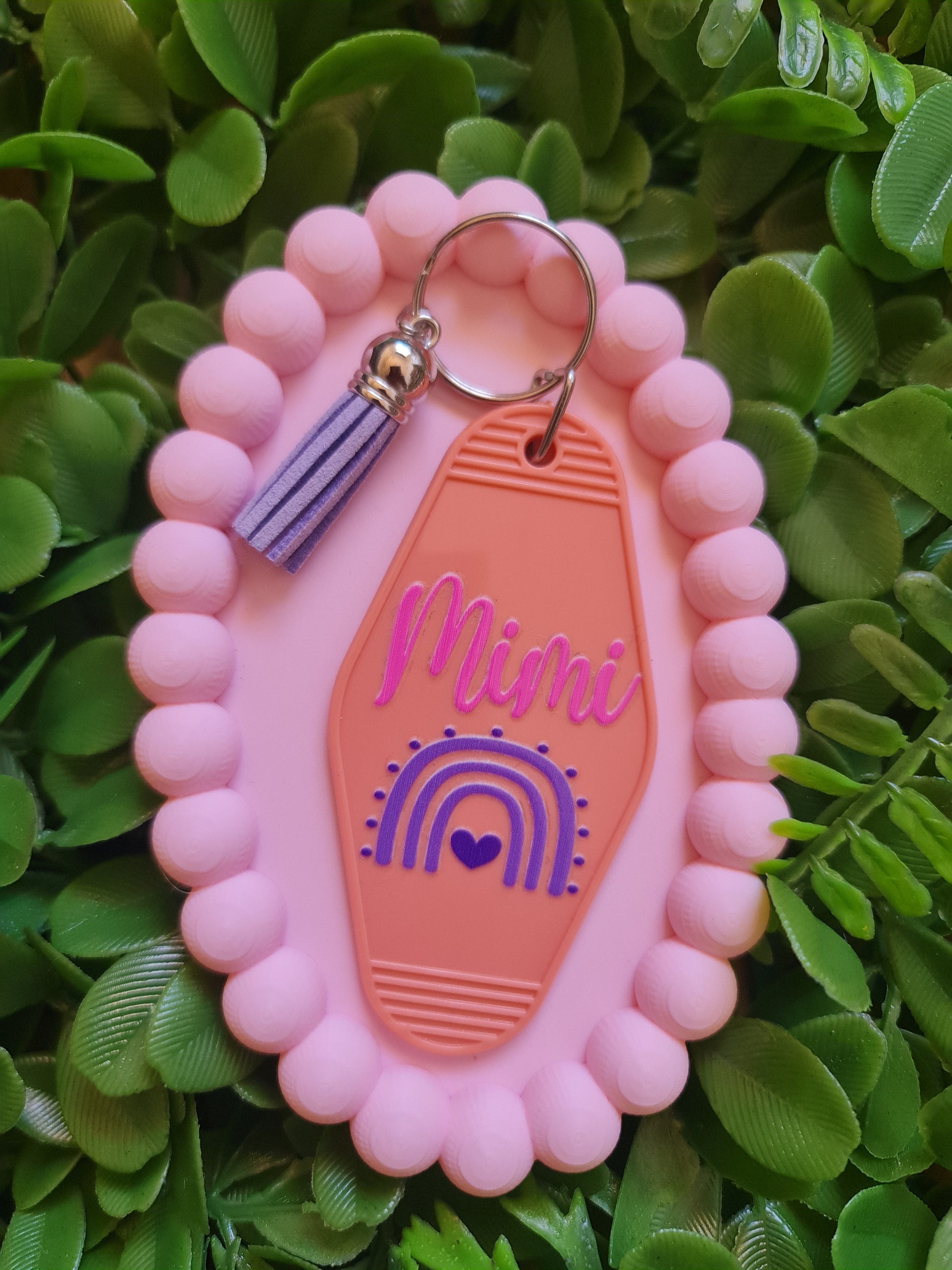 Pink and orange keychain with 'Mimi' branding on a green leafy background