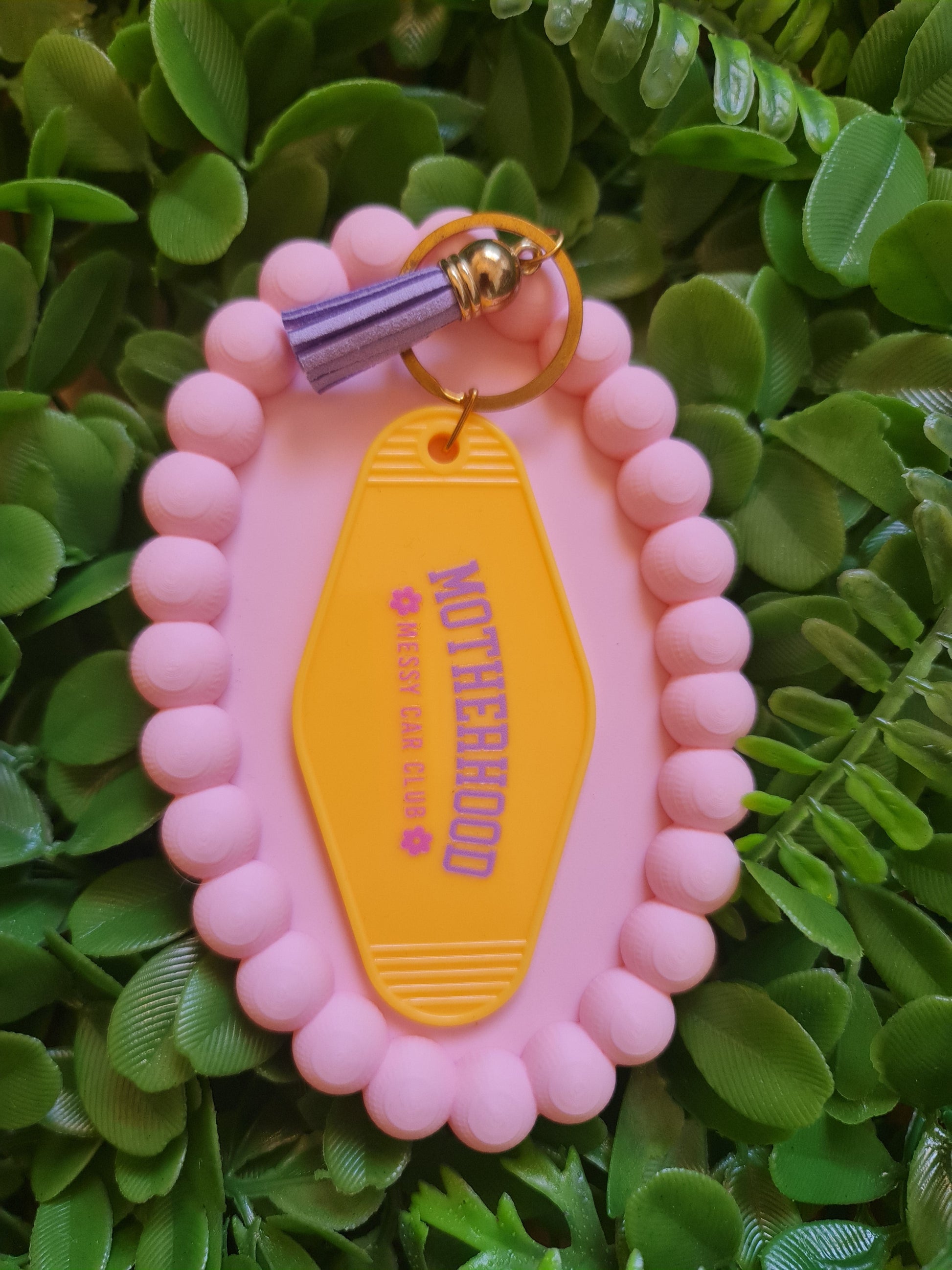 Pink keychain with 'Motherhood' tag on a green leafy background