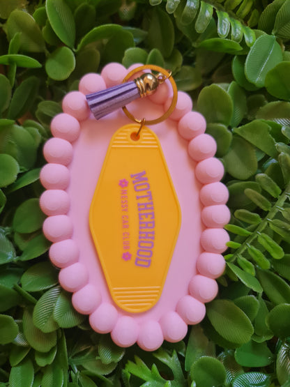 Pink keychain with 'Motherhood' tag on a green leafy background