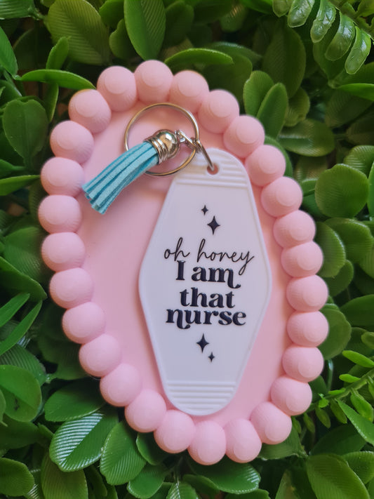 Pink keychain with a white tag and turquoise tassel on a green leafy background