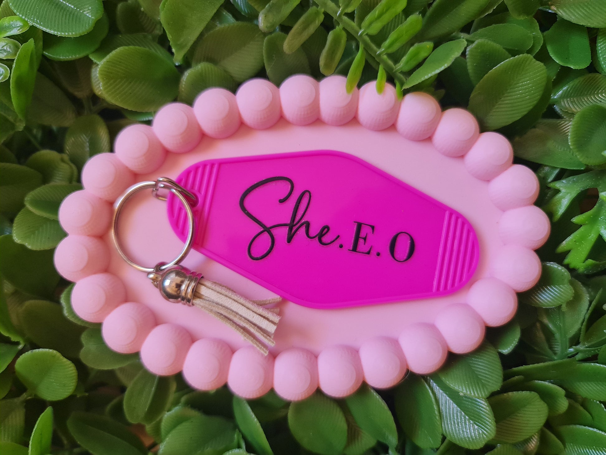Pink keychain with 'She.E.O' on a green leafy background