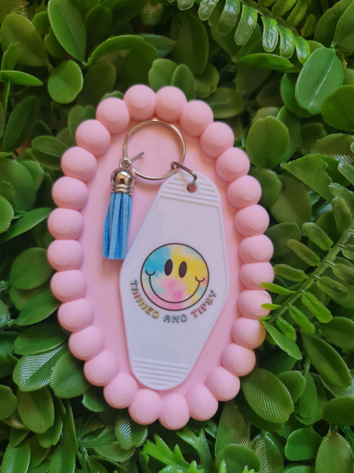 Pink keychain holder with a colorful tag on a green leafy background