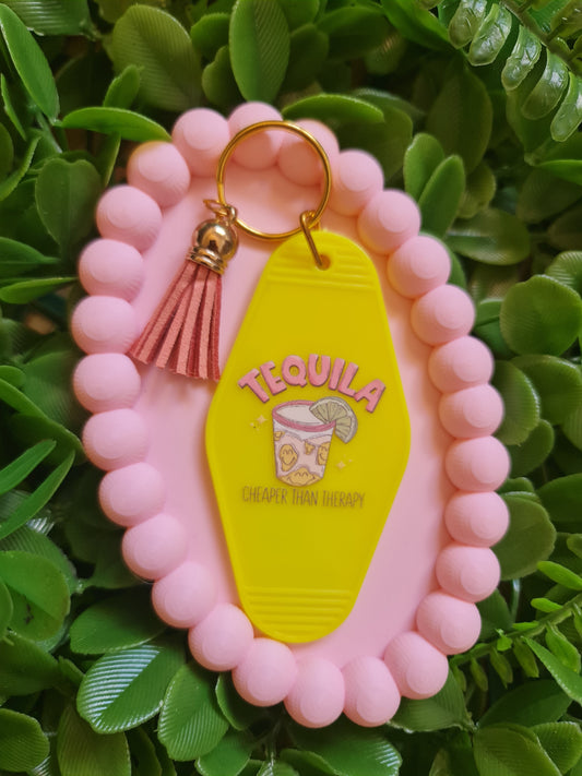Pink keychain with a yellow tequila label on a green leafy background