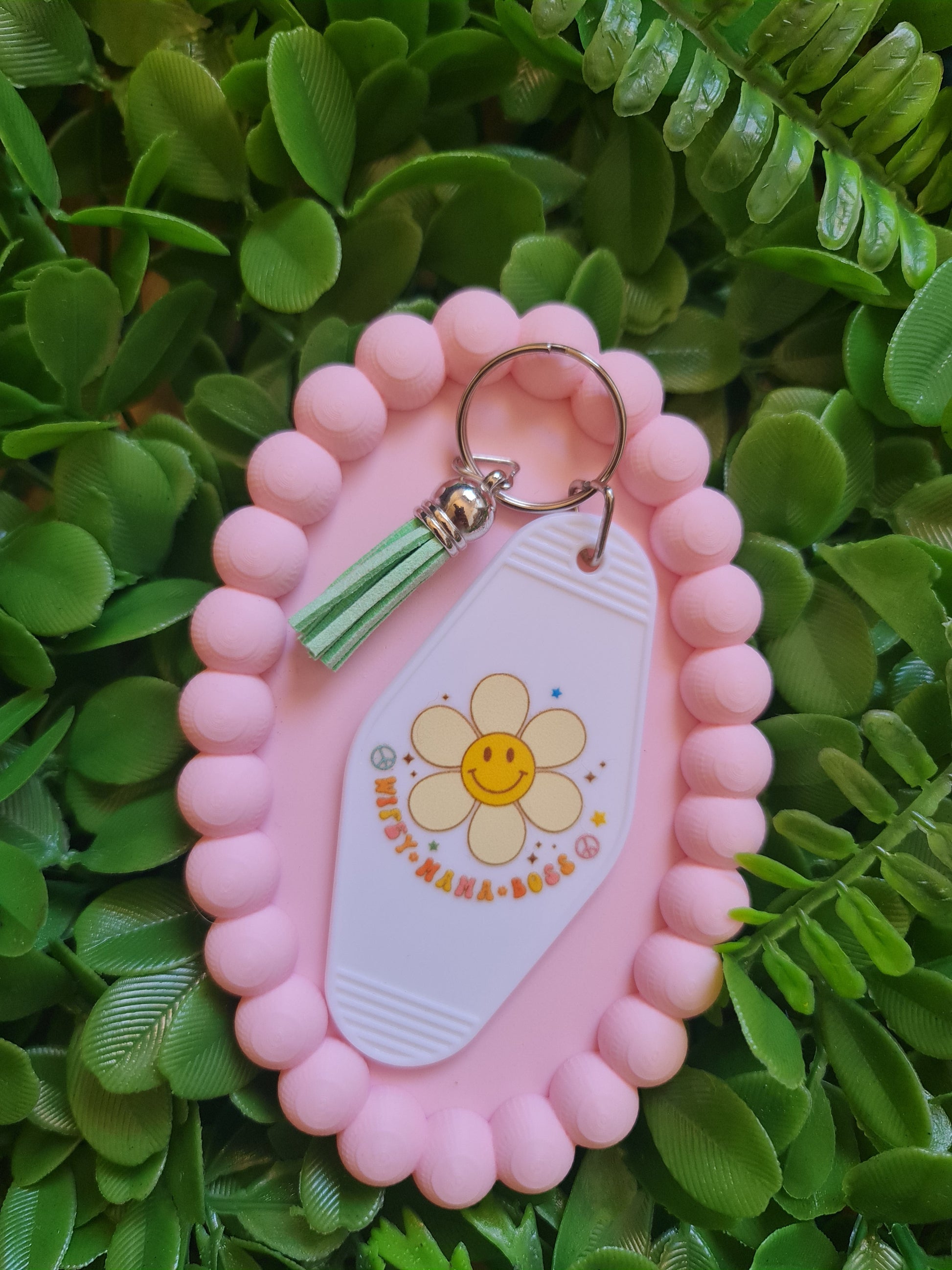 Pink keychain holder with a keychain featuring a flower design on a green leafy background