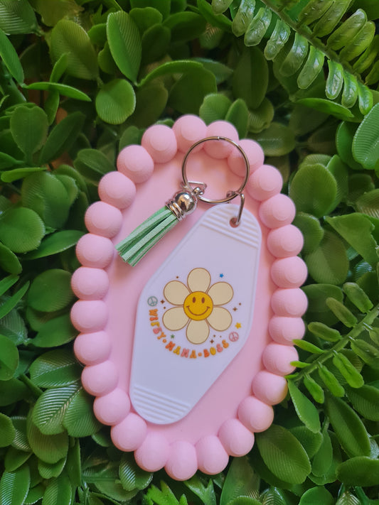 Pink keychain holder with a keychain featuring a flower design on a green leafy background