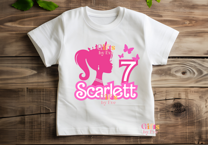 White t-shirt with pink graphics and text on a wooden surface