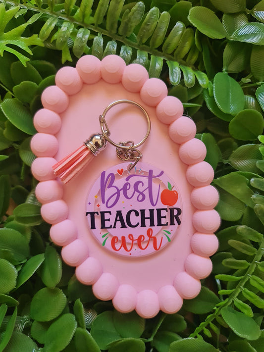 Pink keychain holder with 'Best Teacher Ever' keychain on green leaves