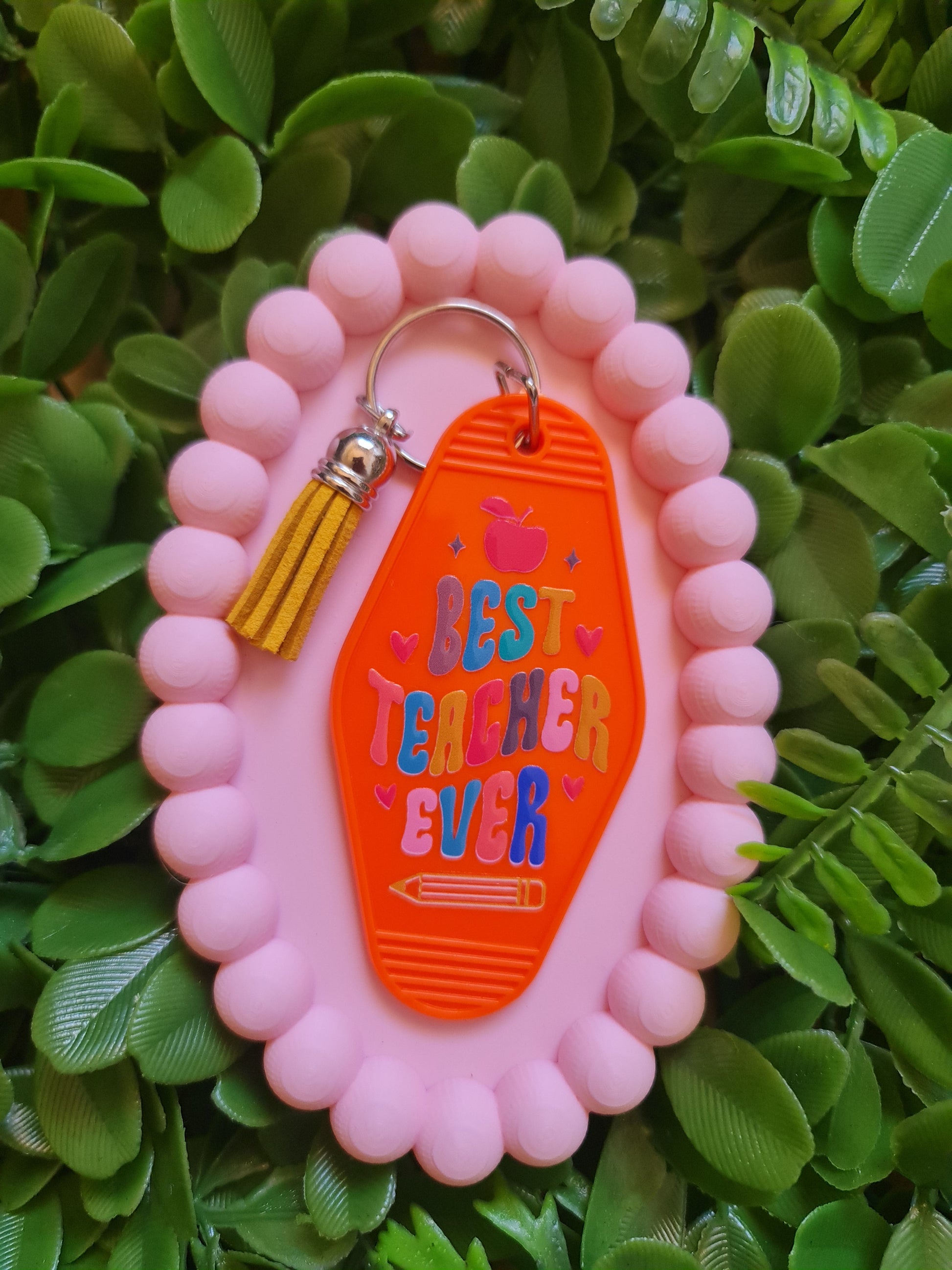 Pink keychain with orange tag on a green leafy background