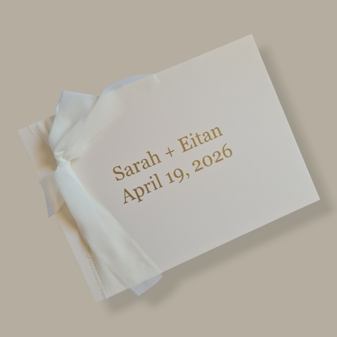 White wedding favor bag with gold text 'Sarah + Eitan April 19, 2026' on a beige background