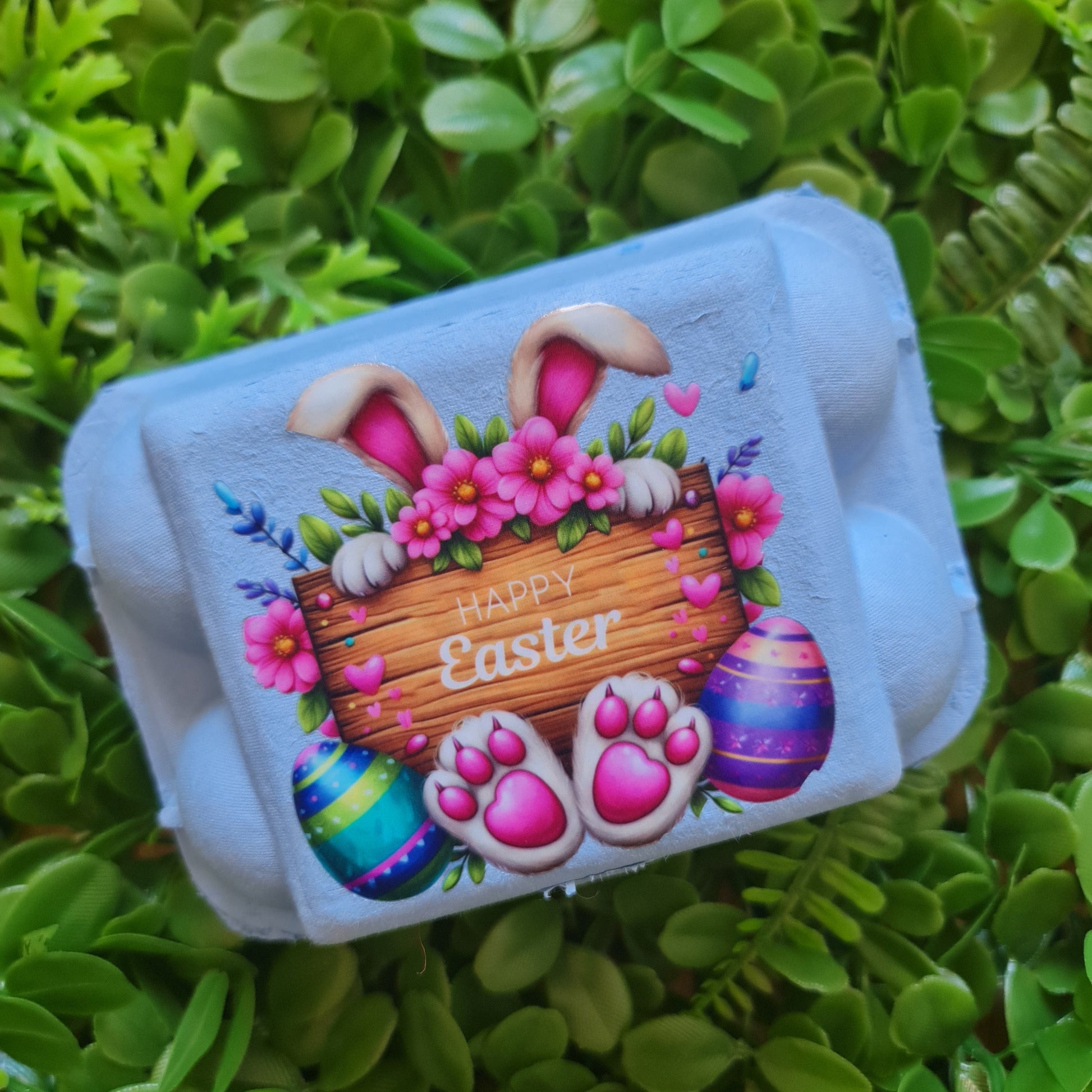 Carton of Easter-themed eggs with a bunny and eggs design on green grass.
