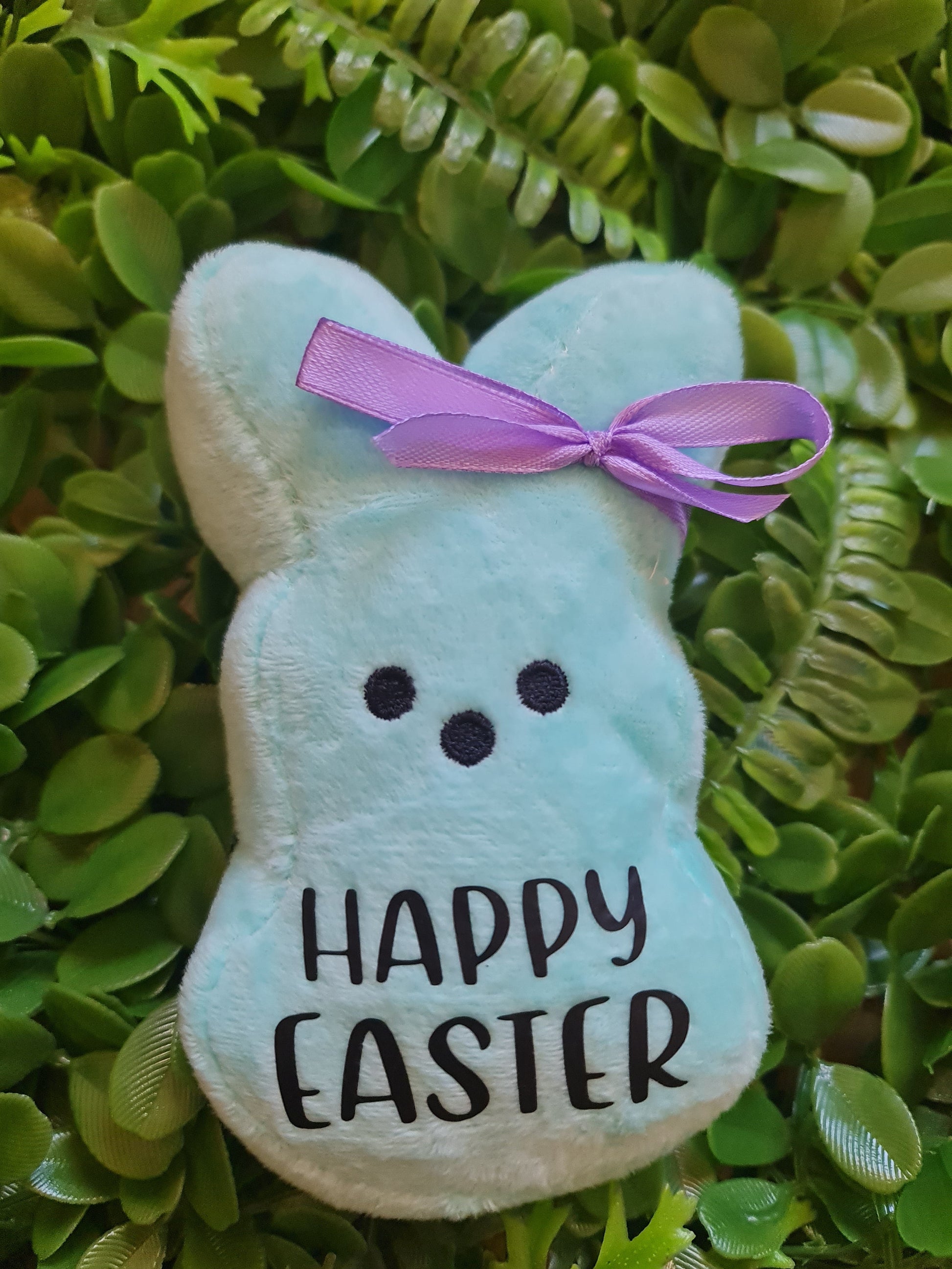 Plush bunny with 'Happy Easter' text and purple bow on green leaf background