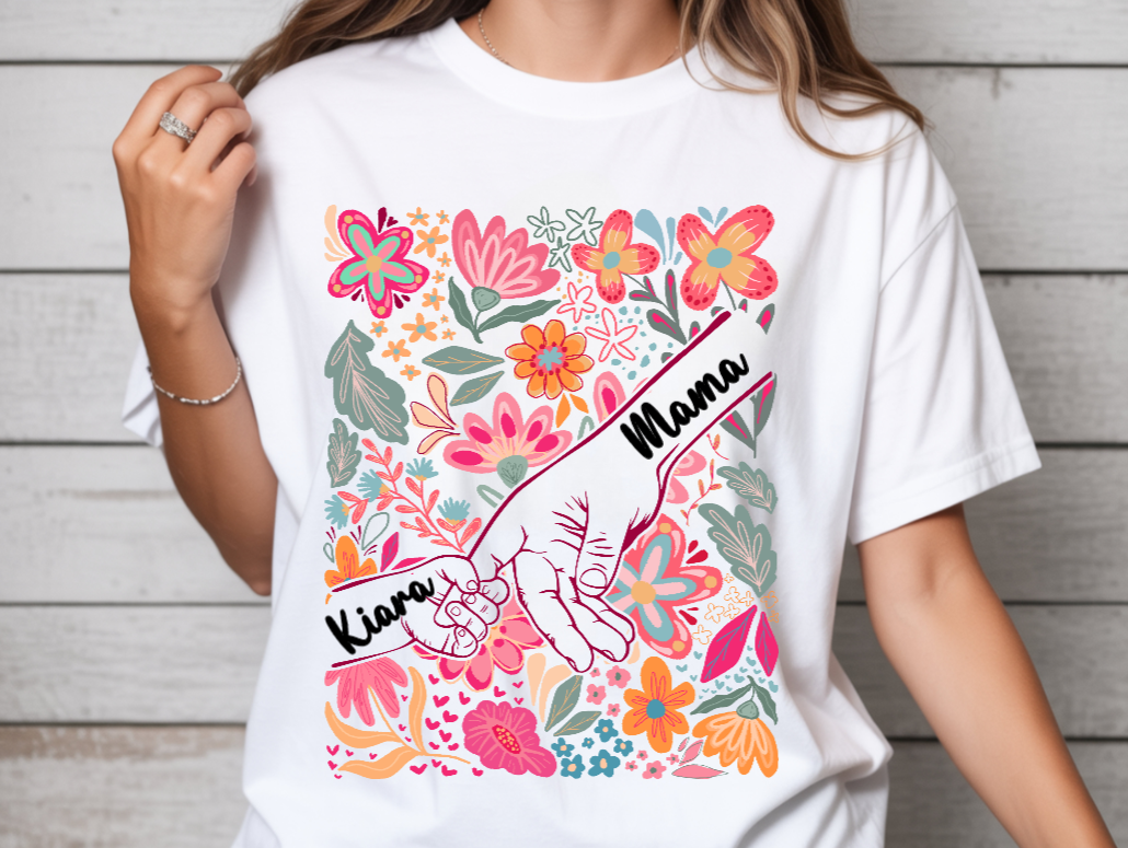 White t-shirt with colorful floral design and 'Mama Kiana' text worn by a person.