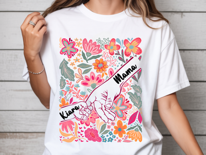 White t-shirt with colorful floral design and 'Mama Kiana' text worn by a person.