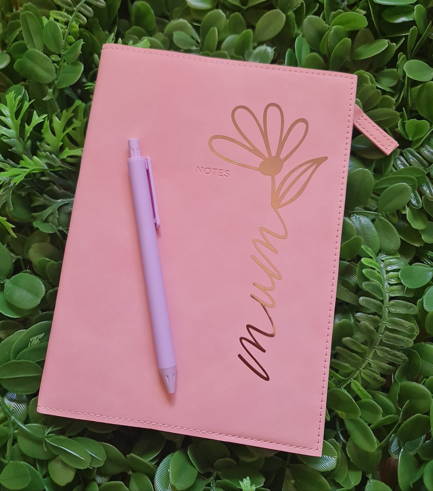 Pink pouch with floral design and pen on green leafy background