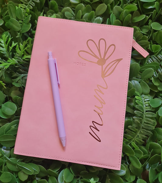 Pink pouch with floral design and pen on green leafy background
