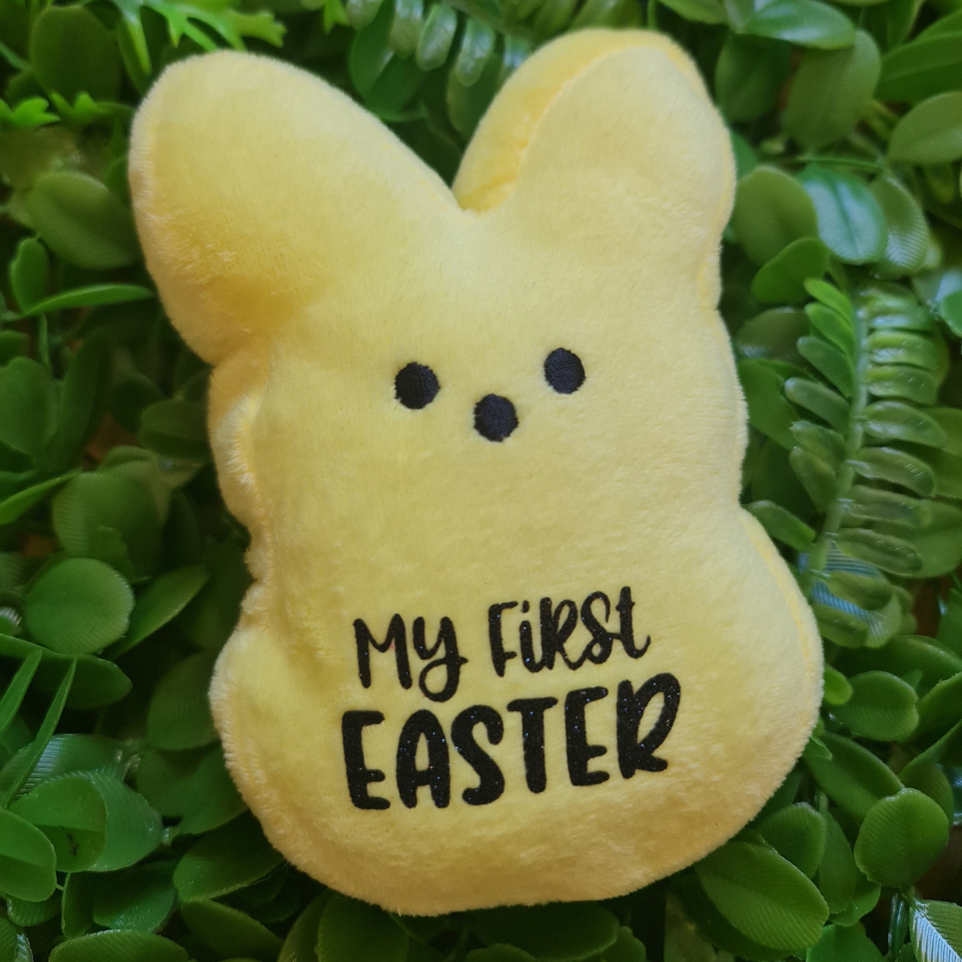 Yellow plush toy shaped like a bunny with 'My First Easter' text on green leaves