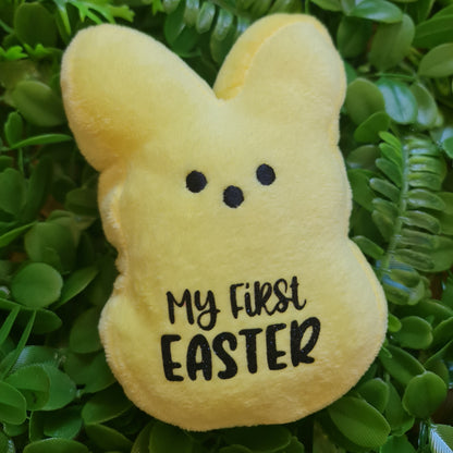 Yellow plush toy shaped like a bunny with 'My First Easter' text on green leaves