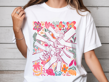 White t-shirt with colorful graphic design of hands and flowers on a wooden background