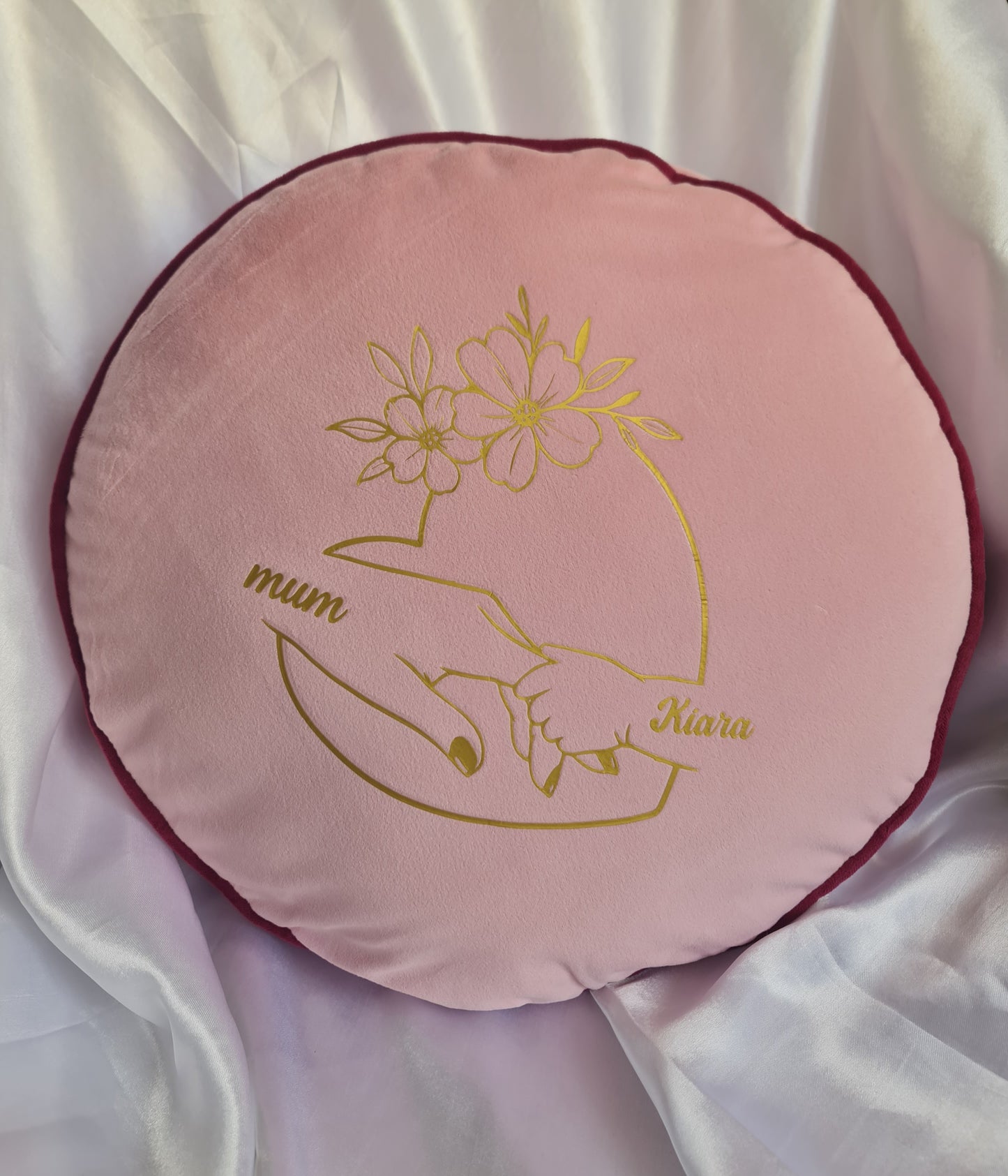 Pink cushion with gold embroidery of hands holding flowers and text on a white background