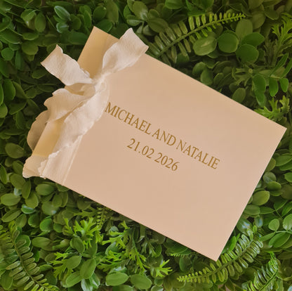 Beige wedding invitation with a white ribbon on green foliage