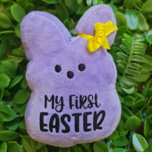Purple 'My First Easter' plush toy with a yellow bow on green leaves