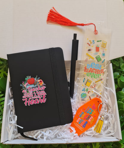 Black notebook with colorful design, pen, and decorative items in a box on grass.
