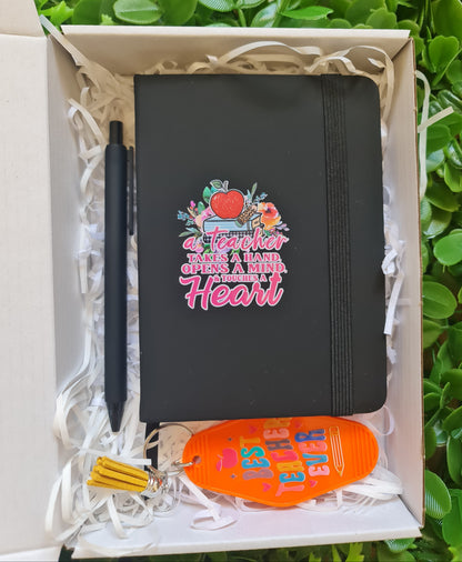Black notebook with colorful design, pen, and keychain in a box on green grass