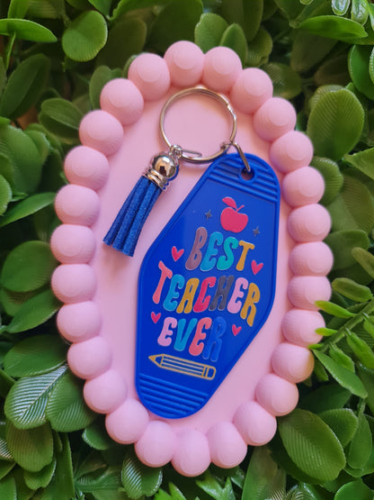 Keychain with 'Best Teacher Ever' text on a pink holder against a green leafy background
