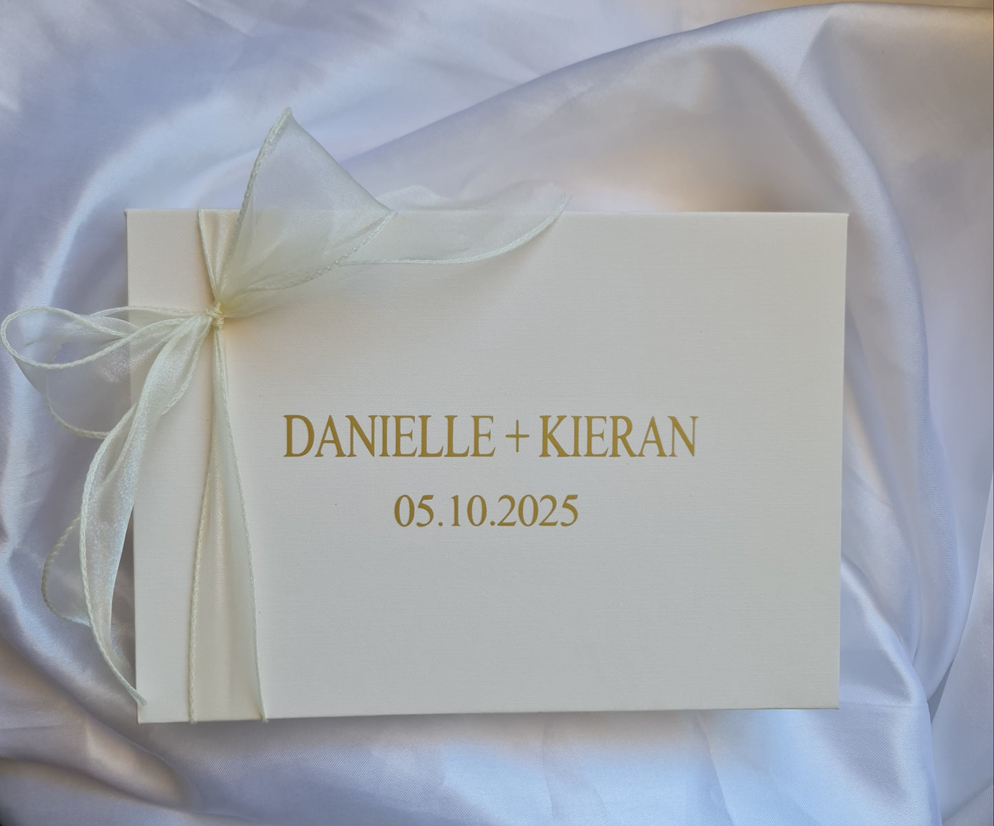 White card with gold text and a bow on a white fabric background