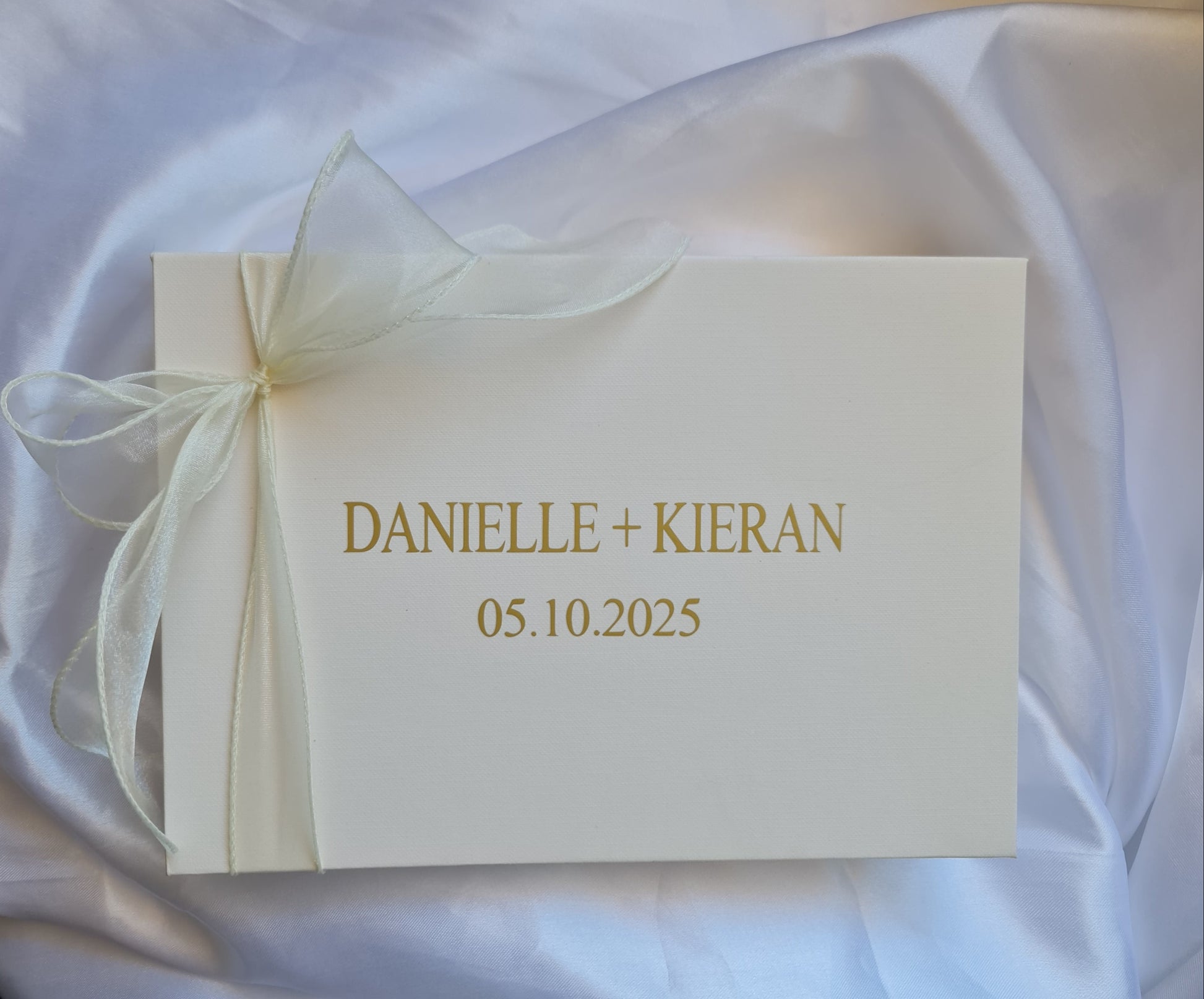 White card with gold text and a bow on a white fabric background